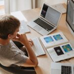 Top view of young programmer working on multiple laptops in a modern office setting.